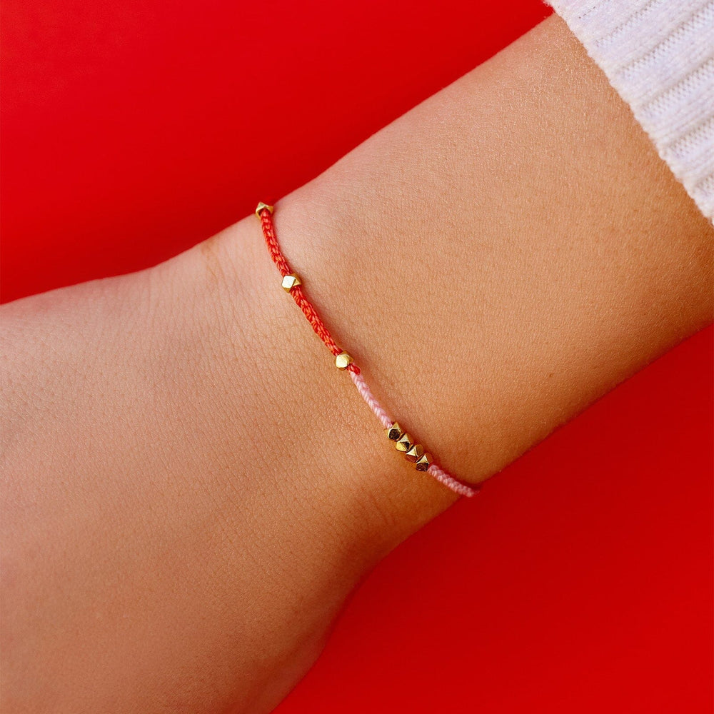 A red string bracelet with a gold-plated cross pendan